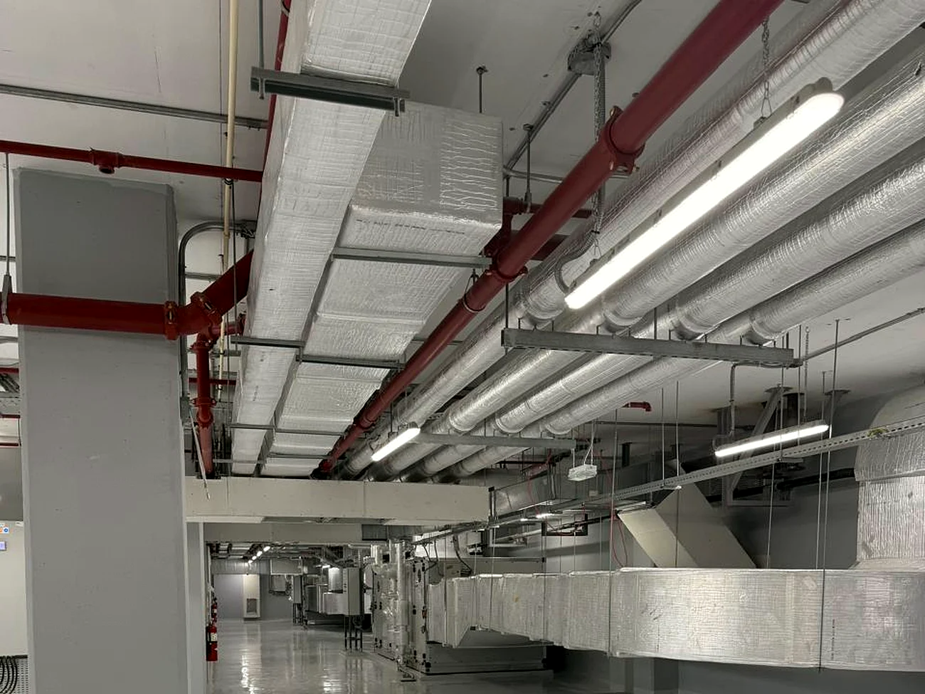 Finished services corridor by Mecamac: insulated ductwork, firefighting mains, cable trays and lighting sharing one ceiling void